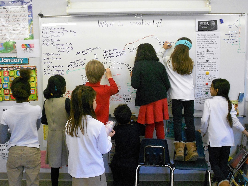 Elementary students writing their definitions of creativity on a white board