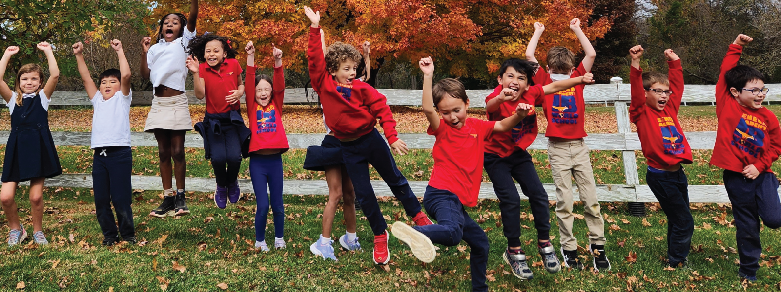 A group of ecstatic elementary students jumping for joy in front of a multicolored tree in the fall