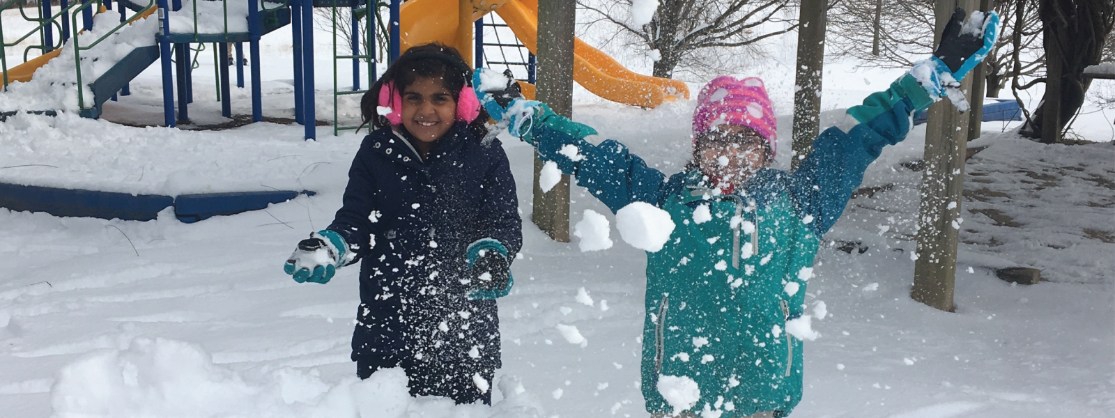 two happy elementary friends bundled up against the cold while they throw snow into the air