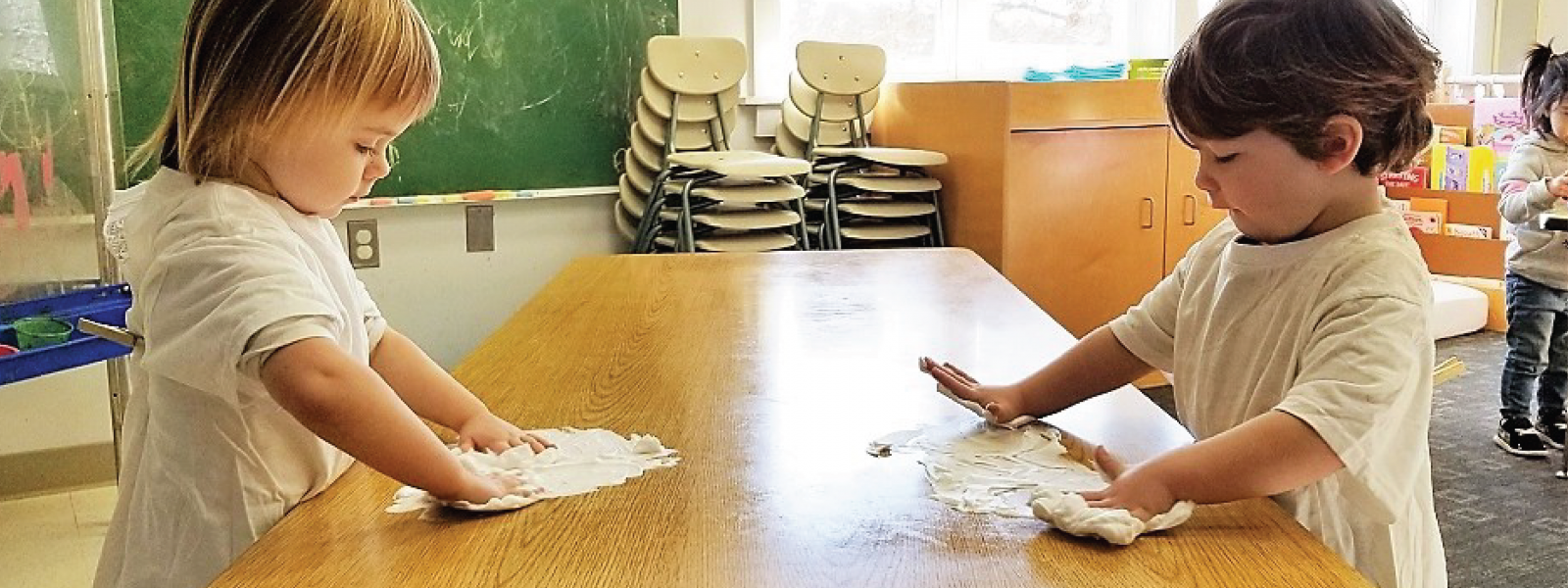 two toddlers playing with shaving cream on either end of a classroom table