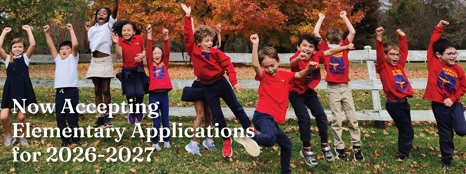 A group of ecstatic elementary students jumping for joy in front of a multicolored tree in the fall
