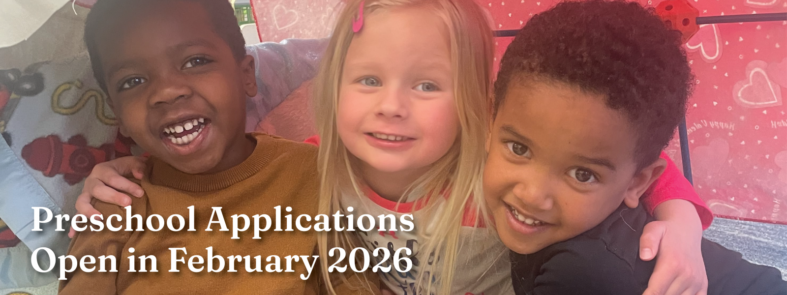 three smiling preschool friends sitting in a blanket fort with their arms around each other