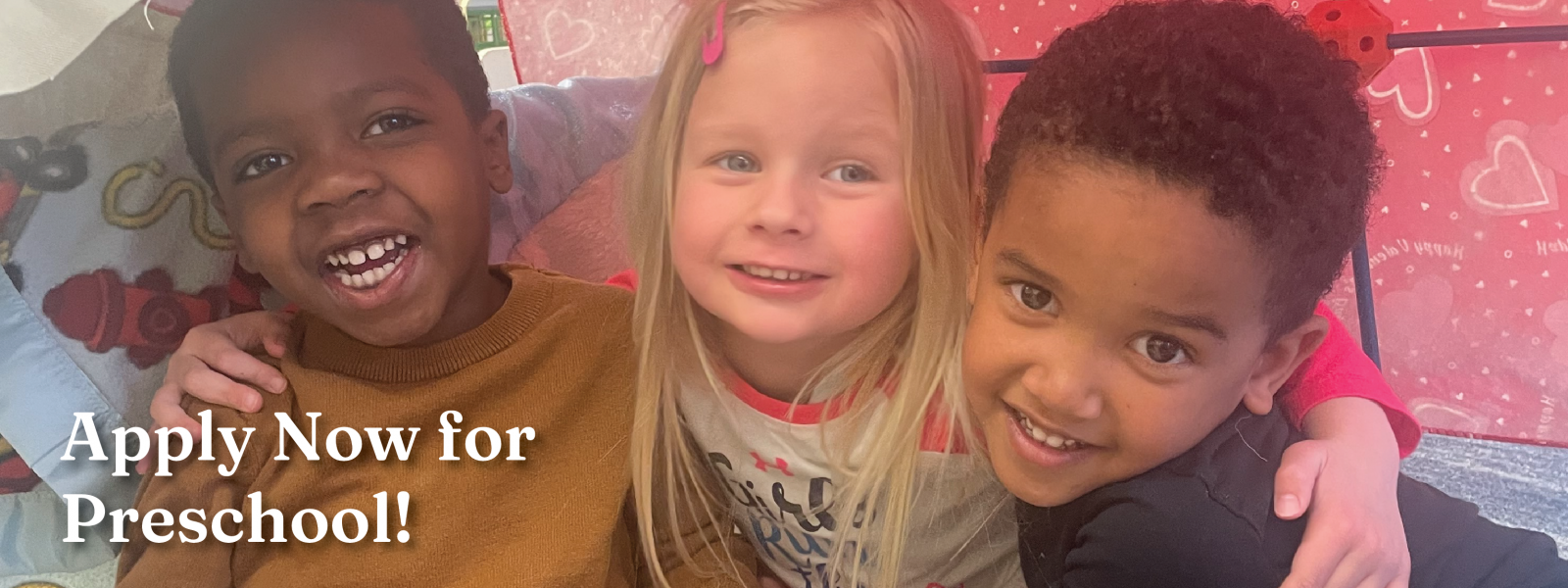 three smiling preschool friends sitting in a blanket fort with their arms around each other